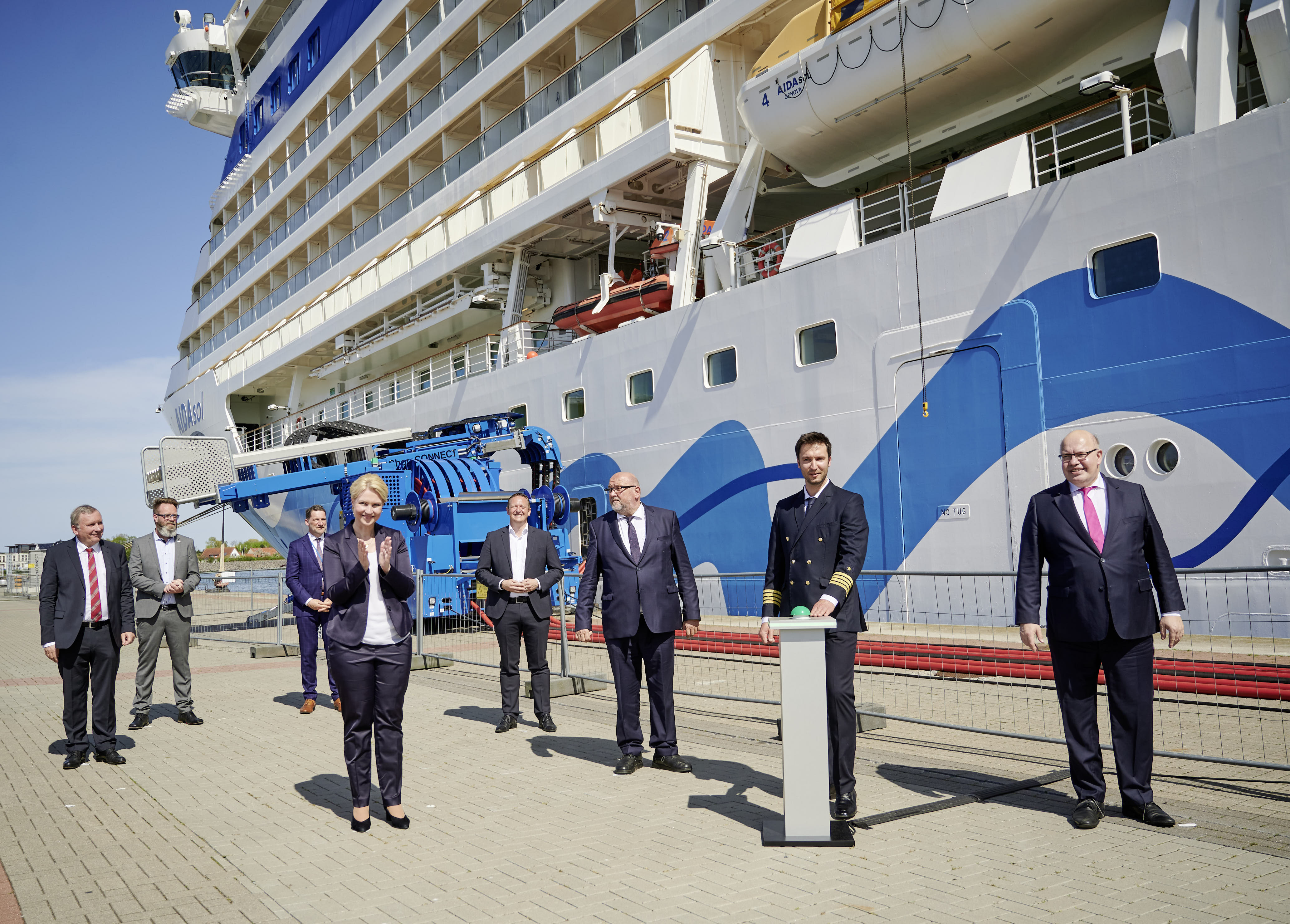 Acht Personen vor einem Kreuzfahrtschiff, die gesamte Gruppe klatscht