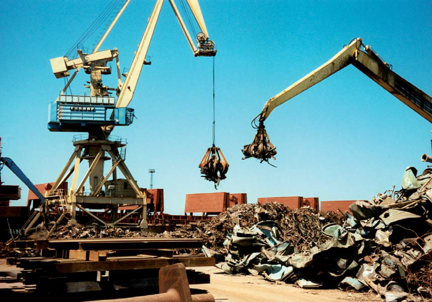 Historisches Archivfoto: Zwei Kräne verladen Metallschrott von einer Lagerfläche auf ein dahinter liegendes Schiff