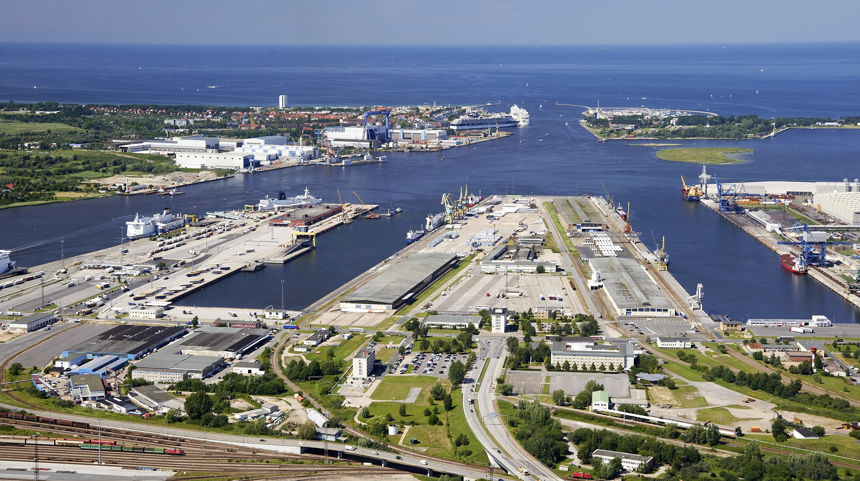 Aerial view of Piers 1 and 2 at the Port of Rostock. Pier 2 with its two quayside warehouses is the main focus, while three ships are berthed alongside.