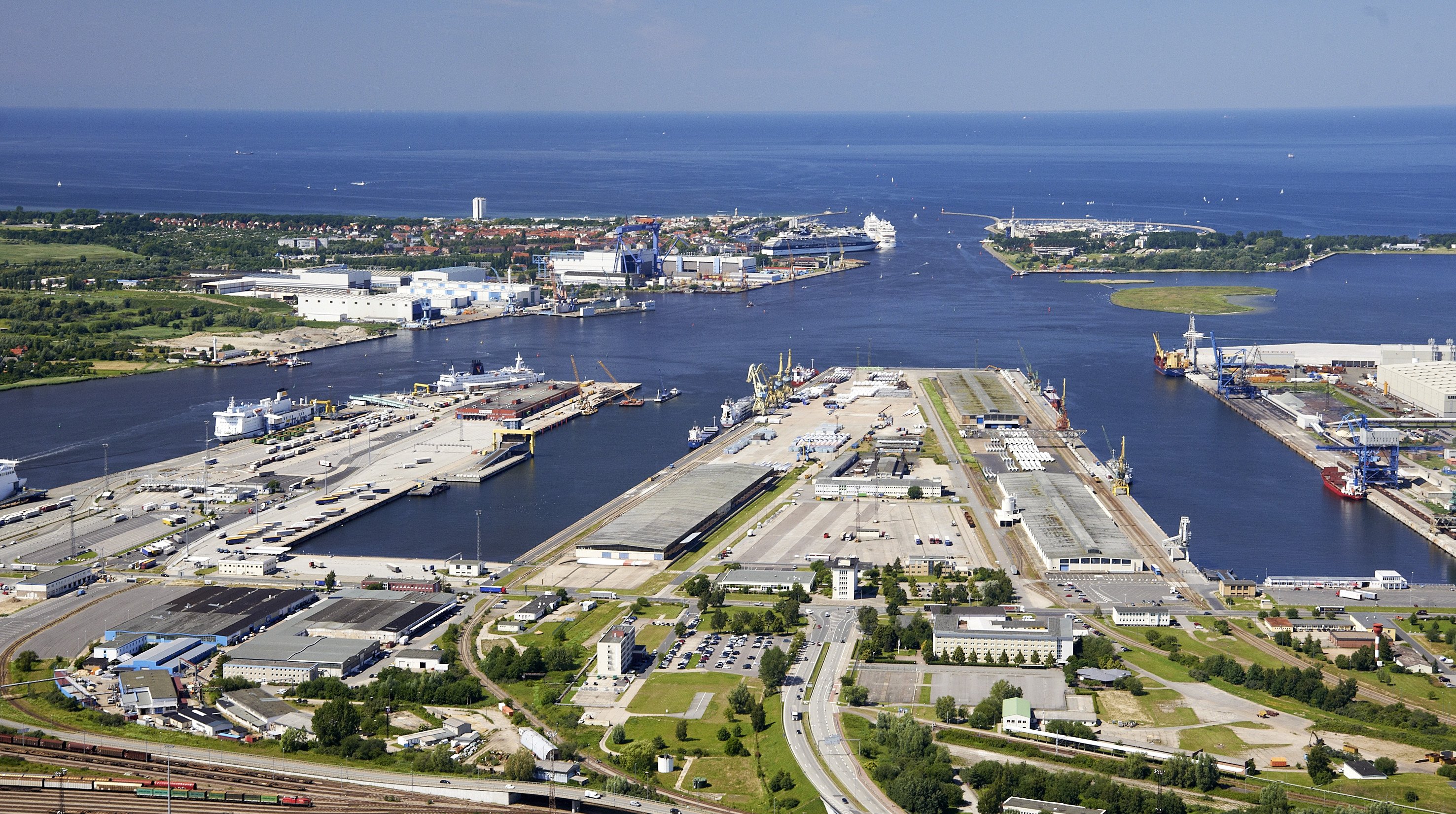 Luftbild von Pier 1 und Pier 2 im Seehafen Rostock. Im Mittelpunkt steht Pier 2 mit zwei Kaihallen, an den Liegeplätzen liegen drei Schiffe.