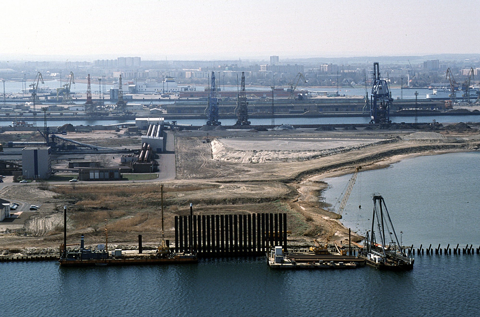 Luftbild von Bauarbeiten und Sandaufschüttungen zur Neugestaltung der Liegeplätze auf Pier 3, mit Kränen und dem Fährterminal im Hintergrund