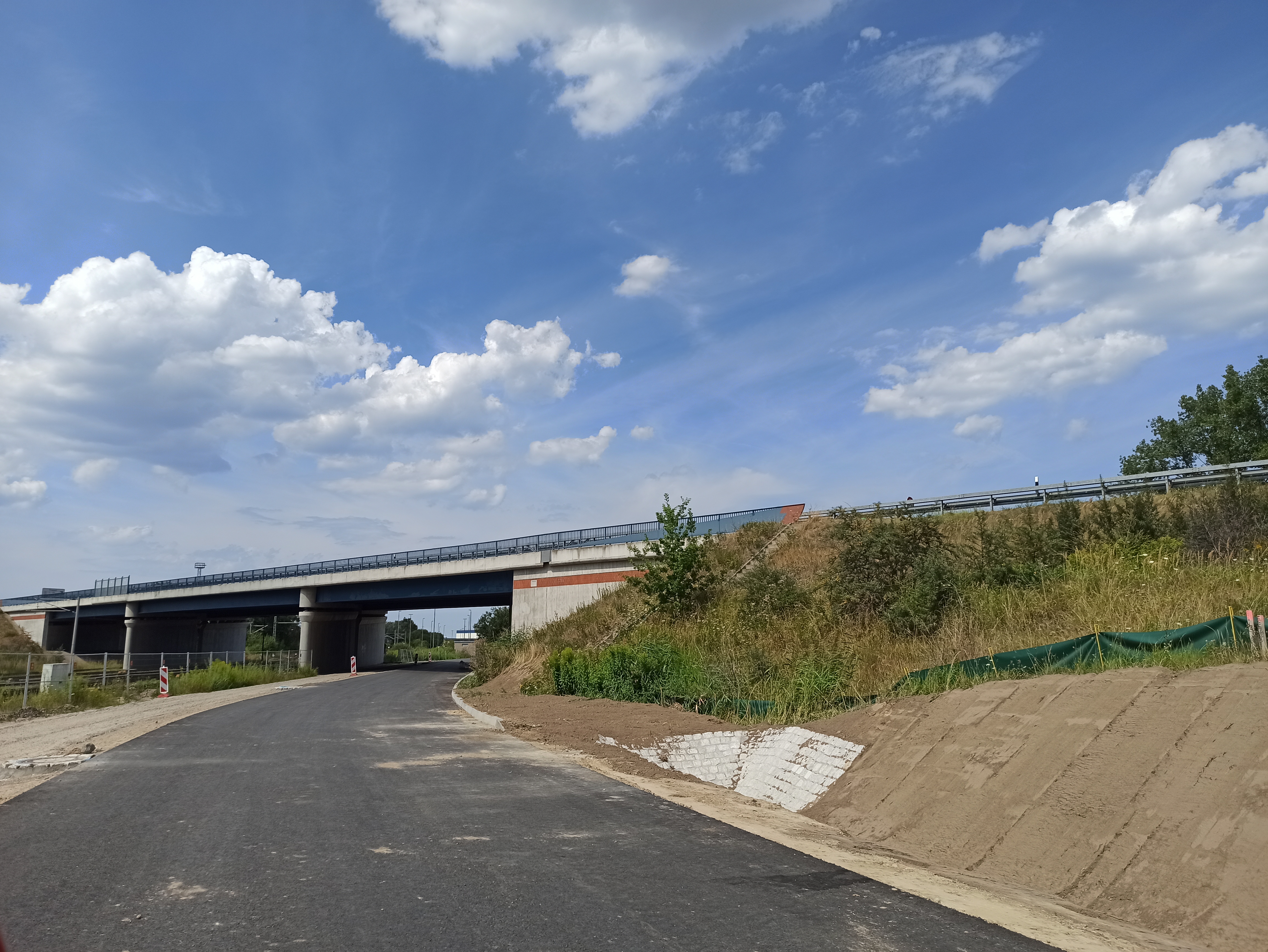 Die neu asphaltierte Zufahrtsstraße zur Autobahnabfahrt „Seehafen Industriehafen“. Der Straßenverlauf führt im Vordergrund direkt unter einer Betonbrücke der Autobahn hindurch.